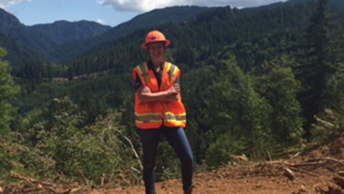 Raelyn stands on worksite in safety vest and hardhat