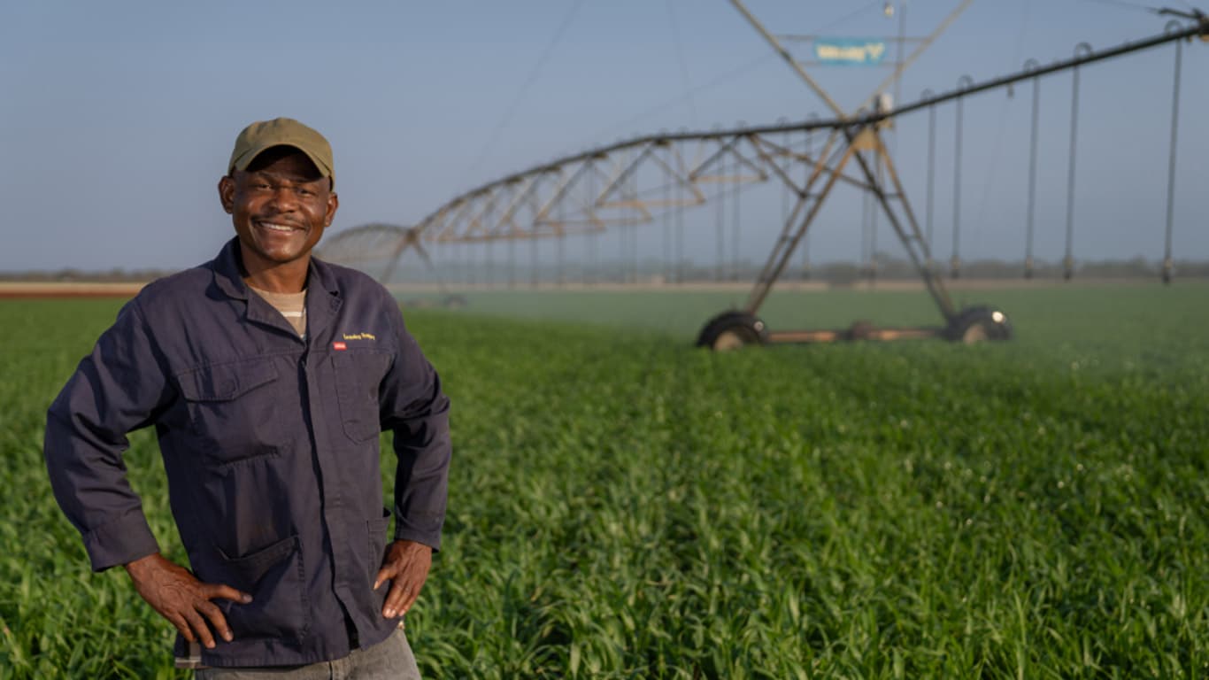 A person stands in a green crop field with a large center pivot irrigation system in the background.